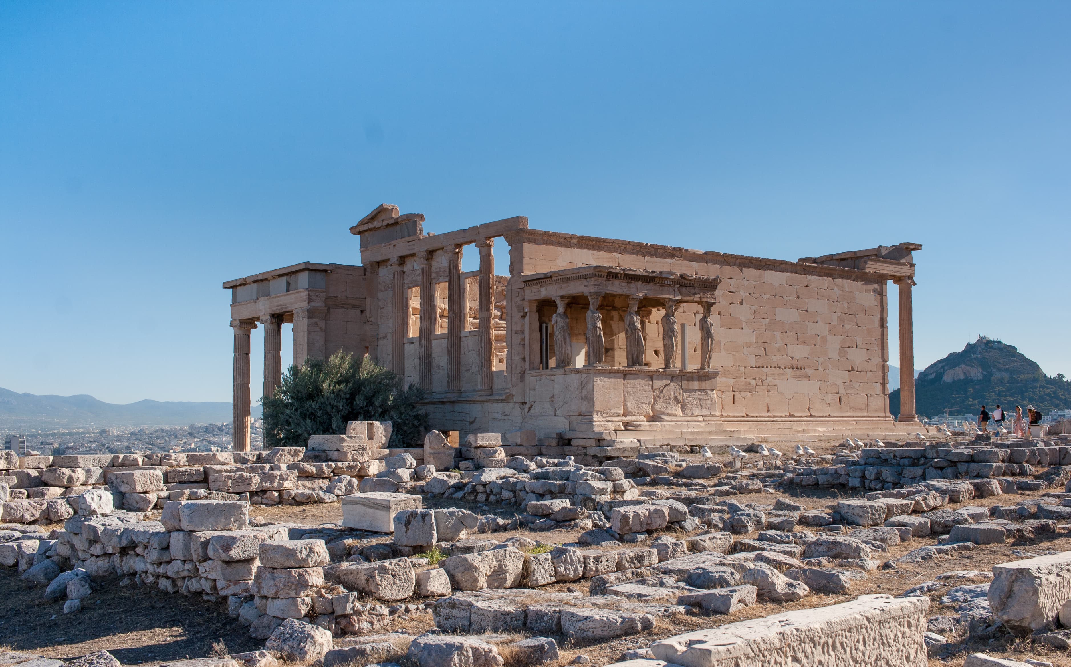 The Erechtheion on the Acropolis with its caryatid porch, Lycabettus Hill visible in the background above the Athens cityscape