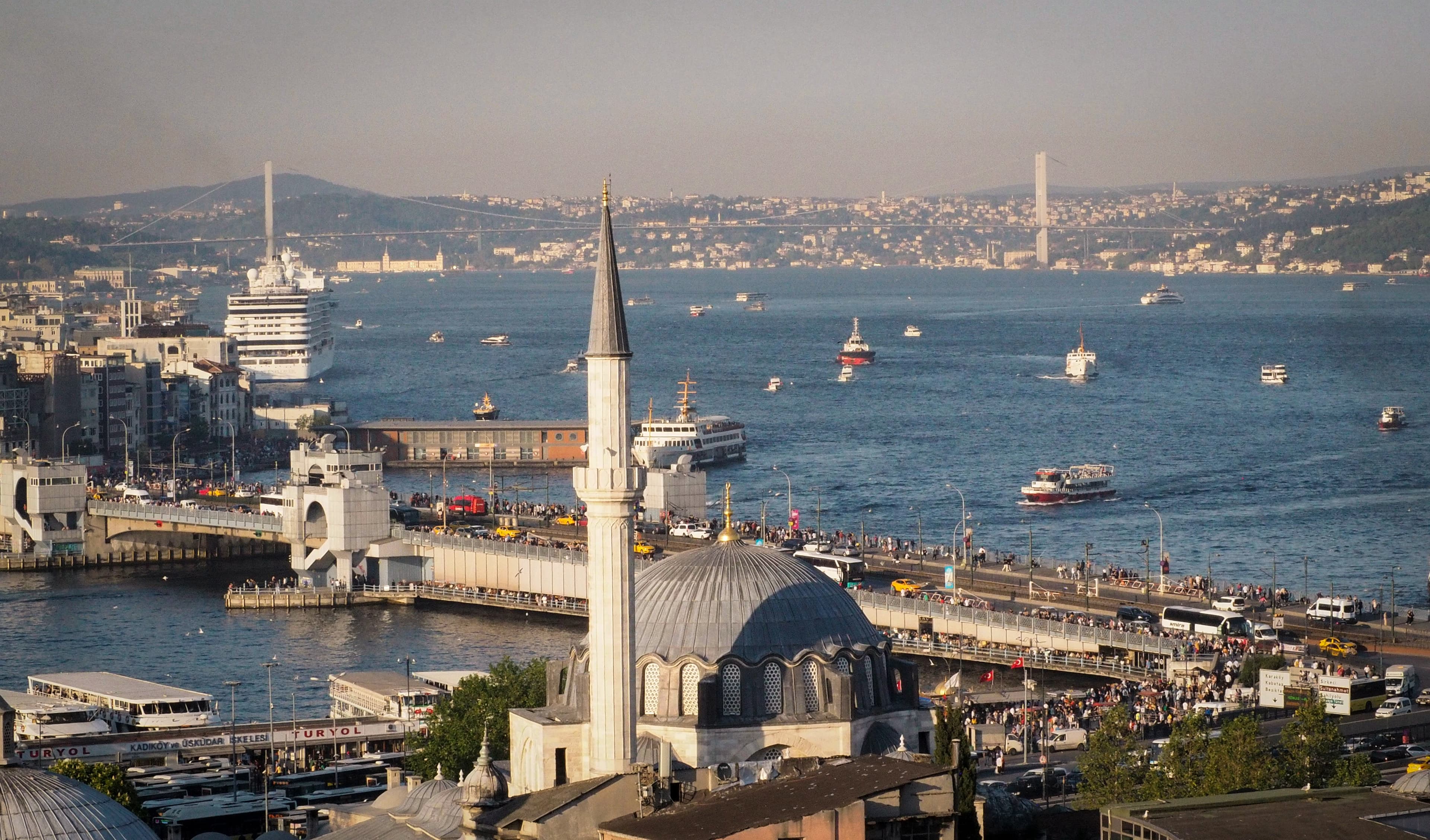 Aerial view from Beyoğlu across the Galata Bridge and the Golden Horn towards the Bosphorus, with ferries crossing the strait and the 15 July Martyrs Bridge - the marathon crossing from Asia to Europe - visible in the distance