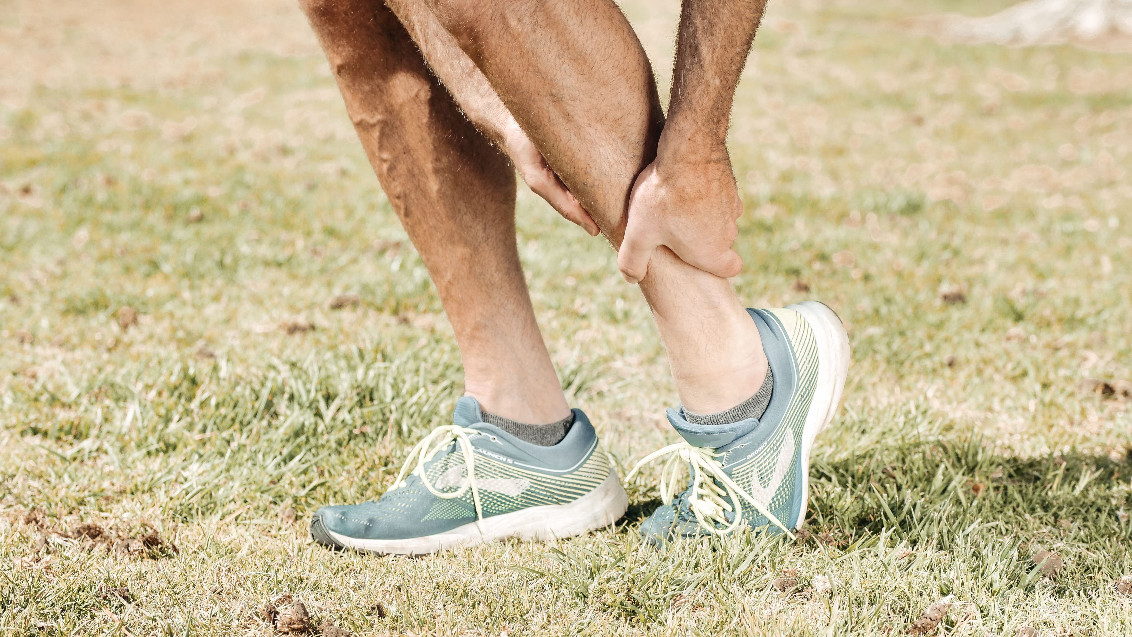 A runner gripping their hamstring during a marathon race, the classic posture of exercise-associated muscle cramping