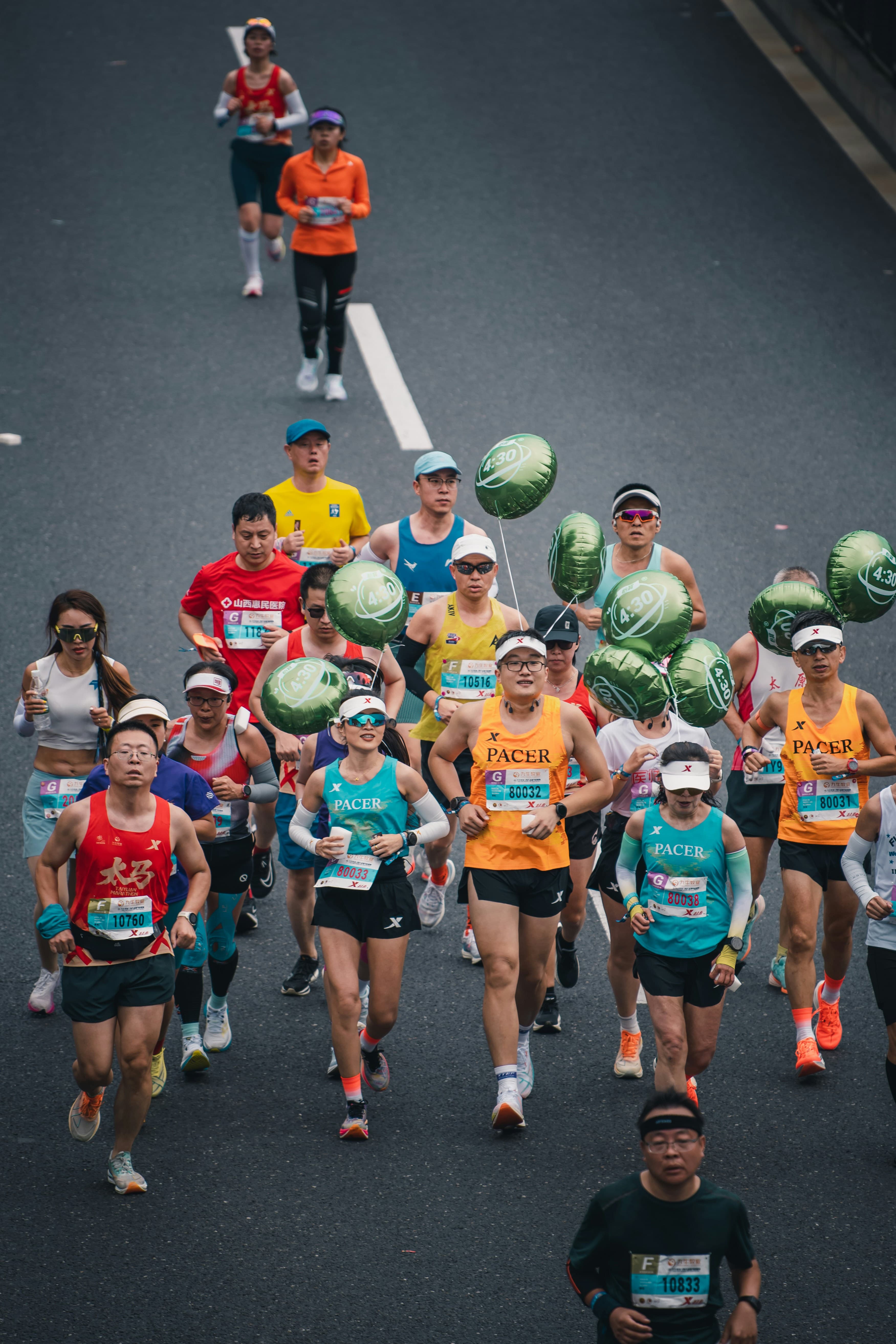 A marathon pacer runner carrying a pace balloon at the head of a large group during a city road marathon